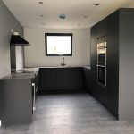 Black kitchen in Vivid Green SIPs annexe featuring built in cupboards, extractor fan, window over sink double oven and charcoal wood flooring
