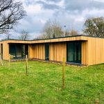 large L-shaped Vivid Green annexe with western red cedar cladding, anthracite grey framed windows and doors, and multiple entrances leading to grassy garden