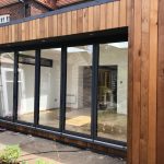 Unfurnished Vivid Green SIPs house extension with two skylights brightening the space, with a western red cedar cladding, anthracite grey bi-fold door and a doorway leading to a room on the left.