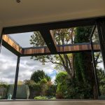 Low angle view from inside a Vivid Green garden office space, featuring anthracite grey aluminum bi-fold doors opening to a cedar and grey trimmed overhang, with the garden in the background.